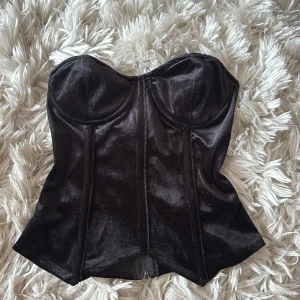 Svart sammetskorsett från Missguided - Supersnygg svart korsett från Missguided i mjuk sammet. Axelbandslös modell med markerade kupor och dragkedja bak. Sitter tajt och ger en riktigt snygg siluett. Perfekt att styla med jeans eller kjol för en cool look.