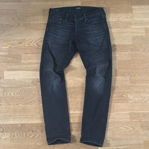 Svarta slim jeans från Jack & Jones - Snygga svarta jeans från Jack & Jones i modellen Slim/Glenn. Jeansen har en slim passform, klassisk femficksdesign och är tillverkade i stretchigt denimtyg för extra komfort. Perfekta för dig som gillar en smal siluett och stilren look.