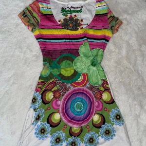 Färgglad midiklänning från Desigual - Superunik kort/midiklänning från Desigual med massor av färger och mönster! Klänningen har korta ärmar, rund halsringning och coola blommiga och randiga detaljer i rosa, grönt, blått och vitt. Perfekt för dig som gillar att sticka ut och vill ha något riktigt färgstarkt. Skulle säga storlek S eller M