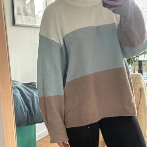 Randig stickad tröja från 157 - Mysig stickad tröja från 157 i oversized modell med breda blockränder i beige, ljusblått och vitt. Tröjan har lång ärm, ribbade muddar och hög hals. Perfekt för lager-på-lager och chill dagar.