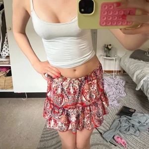 Färgglad volangkjol med paisleymönster - Supersöt kjol med volanger och paisleyinspirerat mönster i rött, blått och orange på vit botten. Kjolen har resår i midjan och är luftig och lätt, perfekt för varma dagar. Passar dig som gillar färg och boho-vibe. 