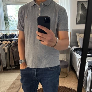 Grå pikétröja Polo Ralph Lauren - Snygg grå pikétröja från Polo Ralph Lauren i slim fit-modell. Klassisk krage, tre knappar och broderad logga på bröstet. Tillverkad i mjuk bomull som känns skön mot huden. Perfekt till jeans eller shorts för en clean och stilren look.