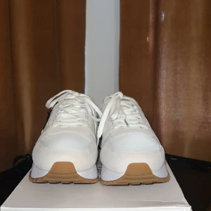 Vita sneakers från Calvin Klein - Snygga vita sneakers från Calvin Klein med beige detaljer och klassisk logga på sidan. Skorna har snörning, platt sula i gummi och ovandel i en mix av skinn och syntet. Perfekta för en clean och stilren look, passar till det mesta i garderoben. Har endast använt de engågn 