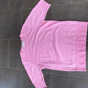 Rosa stickad tröja från Kappahl - Snygg rosa stickad tröja från Kappahl med rund halsringning och ribbade muddar. Modellen har halvkort ärm och är i mjukt material som känns skönt mot huden. Perfekt för dig som gillar en enkel men färgglad stil.