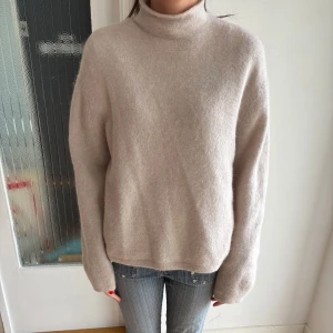 Ljusrosa polotröja från & Other Stories - Supermjuk beige polotröja från & Other Stories, gjord i en lyxig mix av alpacka och ull. Tröjan har en relaxed fit med långa ärmar och hög krage, perfekt för lager på lager. Enkel och stilren design som funkar till allt.