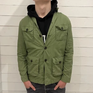 Grön overshirt - Grön overshirt från j lindeberg i strlk S. Modellen på bilden är 180 och väger c 75. Jackan är tunn och passar perfekt nu till sommaren. Jackan har några hål på främre fickan som visas på bilderna men skulle själv påstå att det kan va lite snyggt. Nypris c 2500. 