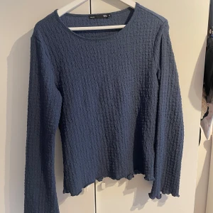 Blå långärmad topp i refflat material - Mörkblå långärmad topp från lager 157 med vågiga kanter vid ärmslut och nederkant. Toppens material är stretchigt och har en strukturerad, krinklad yta som ger en cool look. Perfekt till jeans eller kjol för en chill vibe. Använd  typ en gång.