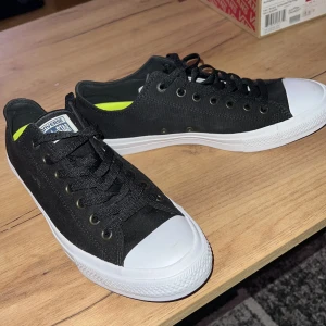 Svarta Converse All Star sneakers - Klassiska Converse All Star sneakers i svart canvas med vita gummidetaljer och bruna sulor. Låg modell med snörning och märkets logga på plösen. Innersulan är limegrön och har Lunarlon-dämpning för extra komfort. Perfekta för en cool och avslappnad stil. Aldrig använda enbart testade