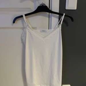 Vit spetslinnetopp från Pieces - Säljer en vit linnetopp från Pieces med tunna axelband och v-ringning dekorerad med spets. Toppen är ärmlös och har en enkel, stilren design som passar perfekt till jeans eller kjol. Materialet känns mjukt och lätt mot huden.