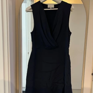 Mörkblå silkesklänning 3.1 Phillip Lim - Supersnygg mörkblå kortklänning i 100% silke från 3.1 Phillip Lim. Klänningen är ärmlös med omlott och v-ringad framtill, vilket ger en elegant och stilren look. Perfekt för dig som vill ha något klassiskt men ändå modernt.