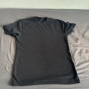 Svart t-shirt från Hugo Boss - Svart t-shirt från Hugo Boss med diskret broderad logga på bröstet. Klassisk rund halsringning och korta ärmar. Tillverkad i 100% bomull för en skön och luftig känsla. Perfekt basic-plagg med stilren vibe.
