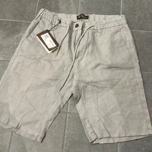 Beige/gråa linneshorts från Loro Piana - Snygga beige/gråa shorts från Loro Piana i lyxigt linne. De har snörning i midjan, diskreta fickor och en clean look som passar perfekt till varma dagar. Klassisk passform och italiensk design gör dem till ett måste i sommargarderoben. Storlek 30, priset går att diskutera 