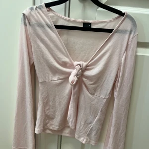 Ljusrosa omlottopp från Gina Tricot - Supersöt ljusrosa topp från Gina Tricot med lång ärm och v-ringning. Toppen har en snygg knut framtill som ger en omlottkänsla och är tillverkad i mjuk bomull. Perfekt för dig som gillar en feminin och trendig stil. Den har en liten fläck men tror att man kan få bort den!🥰