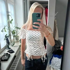 Vit prickig offshoulder topp - Säljer en söt vit offshoulder topp med svarta prickar. Toppen har korta ärmar och snörning framtill som ger en fin rynkad effekt❤️🙏🏽