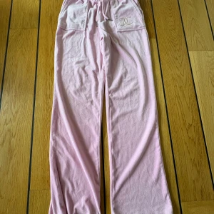 Rosa mjukisbyxor Juicy Couture - Supermysiga ljusrosa mjukisbyxor från Juicy Couture med broderad logga på fickan fram. Byxorna har snörning i midjan, stora fickor både fram och bak samt är gjorda i mjuk fleece-liknande bomullsblandning. Perfekta för chill dagar.