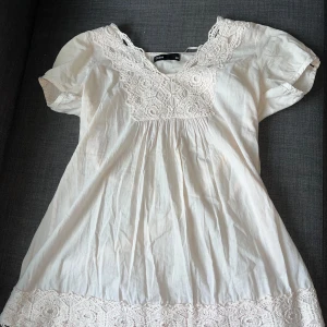 Vit blus med spets från Cubus - Supersöt vit blus från Cubus med v-ringning och fina virkade spetsdetaljer vid halsringning och nederkant. Lätt och luftig bomull, korta puffärmar och avslappnad passform.