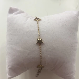 Guldigt armband med stjärnor - Snyggt armband i guldton med små stjärnformade detaljer längs en tunn kedja. Perfekt accessoar för att ge din look lite extra shine. Justerbar längd med kedja och lås. Enkel men ändå unik design som sticker ut. Lite sliten på några av stjärnorna med ser fortfarande bra ut!