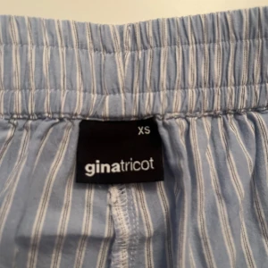 Randiga blå linnebyxor Gina Tricot  - Ljusblå byxor från Gina Tricot i storlek XS. Byxorna har vita smala ränder, resår i midjan och raka, vida ben. På bilden ser det mkt pösigare ut än i vad de gör på, de är raka i passformen och lite luftiga vilket gör de till ett par perfekta ”mjukisar”/pyjamasbyxor(funkar även som alternativ till linnebyxor en varm sommardag)!!! Tyvärr har jag knappt använt de eftersom de är för korta på mig som är ca178