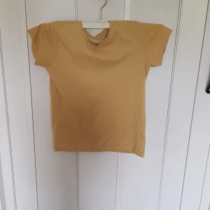 Beige t-shirt från 157 i bomull - Enkel och stilren beige t-shirt från 157 i 100% bomull. Klassisk rund halsringning och korta ärmar, perfekt för en chill och avslappnad look. Passar dig som gillar basic plagg med skön passform.