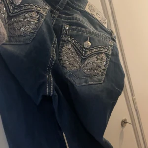 Miss Me jeans med paljettdetaljer - Snygga blå jeans från Miss Me med unika bakfickor dekorerade med broderade vingar och silvriga paljetter. Super trendiga! Inköpta vid jul, andvända ett fåtal gånger sedan dess köptes på raglady för 2299