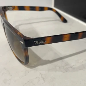Ray-Ban Boyfriend, brunmelerade solglasögon - Snygga Ray-Ban Boyfriend solglasögon med brunmelerat, randigt plastbåge och bruna tonade glas. Klassisk fyrkantig form och ikonisk logga på skalmen. Perfekta för att lyfta din stil med en tidlös vibe. Fodral ingår.