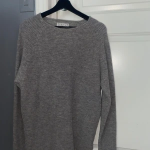 Grå stickad tröja Jack & Jones - Säljer en grå stickad tröja från Jack & Jones Premium. Tröjan har en klassisk rund halsringning och är ribbstickad för en snygg och enkel look. Perfekt för lager-på-lager och passar till allt. Långärmad och mjuk i materialet.