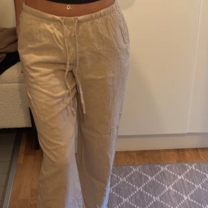 Beiga linnebyxor med snörning - Snygga och luftiga beiga linnebyxor med breda ben och dragsko i midjan. Perfekta för varma dagar och chill vibes. Byxorna har en avslappnad passform och är tillverkade i ett mjukt linnematerial som andas.  Väldigt sällan använda. 