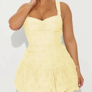 Gul kort klänning med volang - Supersöt gul kortklänning med breda axelband och volangig kjol. Klänningen har broderade blommor i tyget och en smickrande v-ringning. Klänningen är aldrig använd och prislappen sitter på. 