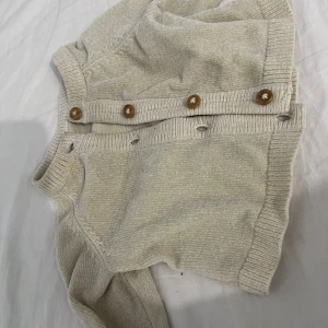 Beige babytröja från Lindex - Söt beige babytröja från Lindex i storlek Newborn. Tröjan har knappar längs sidan för enkel på- och avklädning. Tillverkad av återvunnen polyester, perfekt för de minsta.