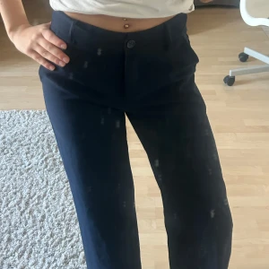 Mörkblå kostymbyxor - Snygga mörkblå kostymbyxor med hög midja och raka ben. Perfekta för en stilren look. Byxorna har knäppning fram och sidofickor för extra funktionalitet.