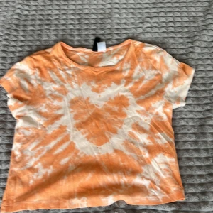 Orange och vit t-shirt med hjärtmönster - Säljer en cool orange och vit t-shirt med ett stort hjärtmönster i mitten. T-shirten har en avslappnad passform och korta ärmar, perfekt för sommardagar. Den är tillverkad i ett mjukt material som känns skönt mot huden.