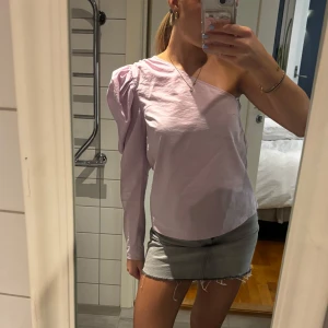 Ljuslila oneshoulder-topp - Säljer en stilren ljuslila oneshoulder-topp med en lång puffärm. Perfekt för en trendig look. Passar bra till både jeans och kjol. Hör av dig vid intresse!