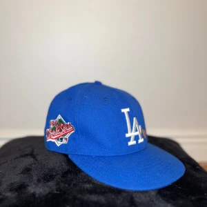 Blå keps med broderad logotyp - Snygg blå keps från New Era med broderad logotyp och text. Kepsen har en 1988 World Series patch på sidan och MLB-logotyp baktill. Perfekt för sportfantaster och samlare.passar bra till den nya trendiga stilen grisch/laidback.