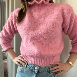Rosa stickad tröja med hög krage - Säljer en mysig rosa stickad tröja med hög krage. Tröjan har långa ärmar och en ribbad kant vid ärmslut och nederkant. Perfekt för kyliga dagar men inte så tjock att man inte kan vandra runt i den på en sommarkväll. Kan bäras i S och möjligtvis XS.