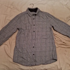 Rutig skjorta från Kappahl - Säljer en stilren rutig skjorta från Kappahl i svart och vit. Skjortan har långa ärmar och knappar framtill. Den är helt oanvänd, då den inte passade. Perfekt för en klassisk look.