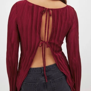 Vinröd topp med öppen rygg och knytband - Snygg vinröd topp med ribbad textur och öppen rygg som knyts med band. Långärmad design med en elegant och modern look. Perfekt för att sticka ut i mängden! Dessutom använd 1 gång! Stolek M och nypris 399. 