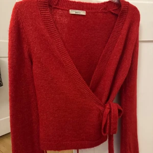 Röd omlottkofta från Gina Tricot - Säljer en snygg röd omlottkofta från Gina Tricot i premiumkvalitet. Koftan har långa ärmar och ett knytband i midjan för en stilren look. Perfekt för att hålla sig  trendig.