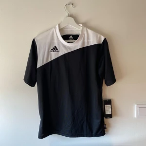 Svart och vit fotbollströja  - Snygg fotbollströja från Adidas i svart och vitt. Tröjan har korta ärmar och en stilren design med Adidas-loggan på bröstet. 