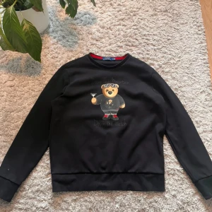 Ralph Lauren bear  - Säljer denna Ralph Lauren Polo Bear sweatshirt i storlek L kan även passa M. En ikonisk tröja med ett stilrent och roligt tryck, perfekt för dig som vill ha en soft och avslappnad look med en touch av lyx.  Detaljer:  Trycket är fortfarande i toppskick  Mjuk och bekväm, perfekt för vardagsbruk  Svart färg med coolt Polo Bear-motiv