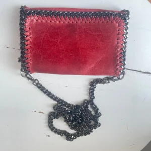 Äkta läder axelväska med kedjedetaljer  - Snygg röd axelväska i läder med coola kedjedetaljer runt kanterna och en kedjerem. Perfekt för att ge din outfit en edgy touch. 