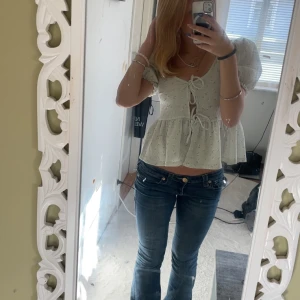 Vit blus från Gina Tricot - Säljer en söt vit blus från Gina Tricot med korta puffärmar och knytning framtill. Blusen har ett diskret blommönster och volangdetaljer som ger en romantisk känsla. Perfekt för vår och sommar!