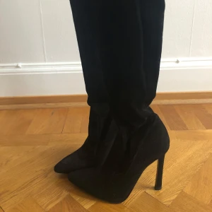 Svarta stövlar med klack - Snygga svarta stövlar i mocka med hög klack och spetsig tå. Perfekta för en elegant look. De är knähöga och ger en stilren siluett.