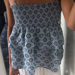 Blå mönstrad linnetopp från Gina Tricot - Säljer en söt blå mönstrad linnetopp från Gina Tricot. Toppen har smala axelband och volanger som ger en fin detalj. Perfekt för varma sommardagar!