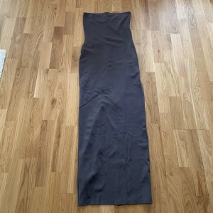 Mörkgrå långklänning  - Snygg mörkgrå långklänning från NA-KD i storlek XS. Klänningen har en stilren design med en slits baktill och är axelbandslös. Perfekt för en elegant look.