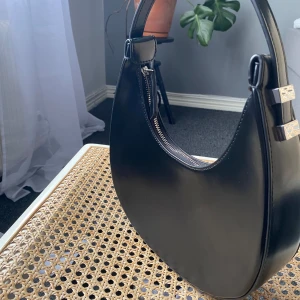 Svart axelväska med dragkedja - Snygg svart axelväska i skinnimmitation med en stilren design. Jättefint skick enda tecknet på användning är en liten repa.