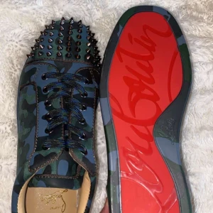 Loubs  - Snygga sneakers i camouflage-mönster från Christian Louboutin med ikonisk röd sula. Skorna har nitar på ovandelen och snörning framtill. Perfekta för att den trendiga Grisch stilen. ⚠️OBS: Vet ej om de är äkta.