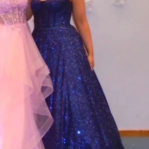 Mörkblå glittrig balklänning - Elegant mörkblå balklänning med glittrande detaljer. Klänningen har en åtsittande överdel med smala axelband och en vid kjol som ger en vacker silhuett. Perfekt för en glamorös kväll. Storlek 38 men sitter 36 också. Skriv för frågor💕 Priset kan diskuteras.