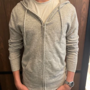 Grå kashmir hoodie från John Henric - Säljer en stilren grå hoodie i mjuk kashmir från John Henric. Tröjan har dragkedja och långa ärmar med ribbade muddar. Perfekt för en avslappnad och bekväm stil. 🧥