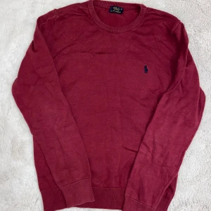 Vinröd tröja från Polo Ralph Lauren - Snygg vinröd tröja från Polo Ralph Lauren med rund halsringning och broderad logga på bröstet. Tröjan har långa ärmar och ribbade muddar vid ärmslut och nederkant. Perfekt för en stilren look.