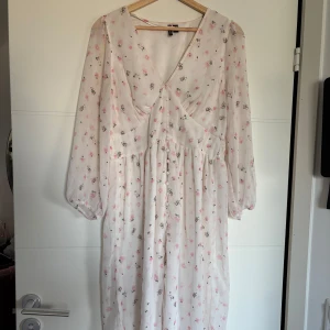 Vit blommig klänning med v-ringning - Säljer en söt vit klänning med blommigt mönster i rosa. Klänningen har en v-ringad och långa ärmar i ett lätt och luftigt material. Perfekt för vår och sommar!